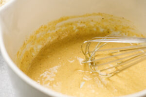 Mayonnaise whisked with crab cake seasoning in a large mixing bowl with a whisk.