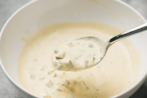 A spoon scooping homemade tartar sauce from a white bowl.
