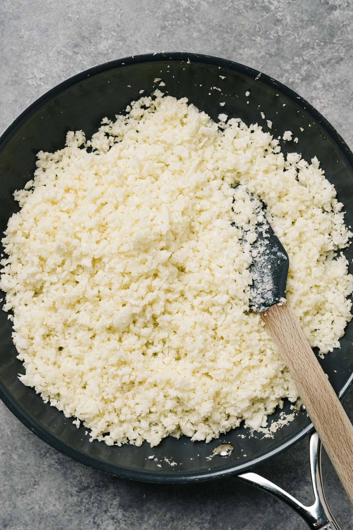 Fresh cauliflower rice sautéing in a skillet with a rubber spatula.