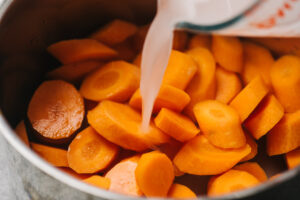 Pour water mixed with cornstarch over sliced carrots in a pot.