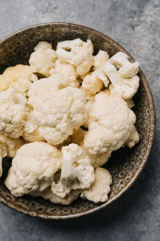 Cauliflower florets in a brown speckled bowl on a concrete background.