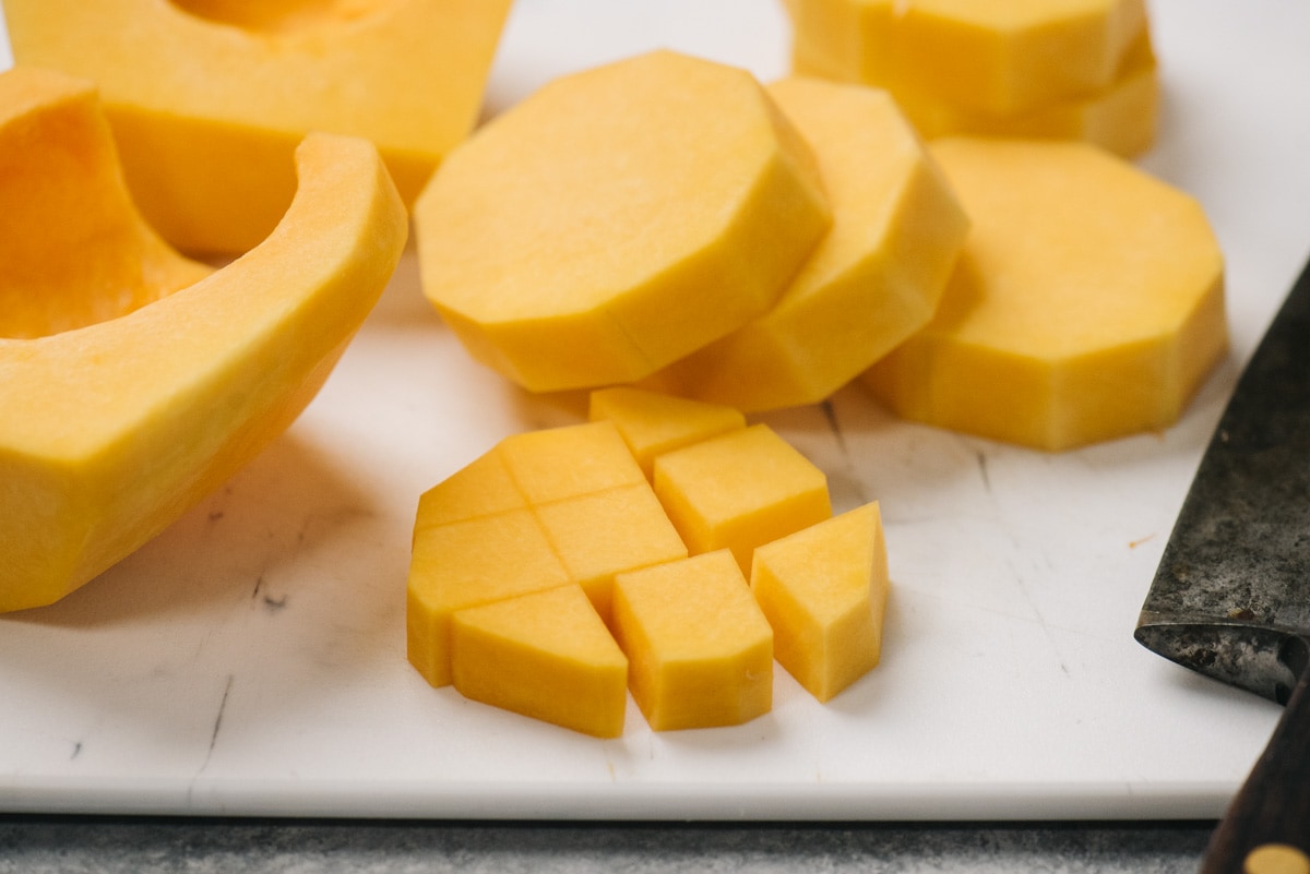 Thick slices of butternut squash on a cutting board and diced pieces next to it.