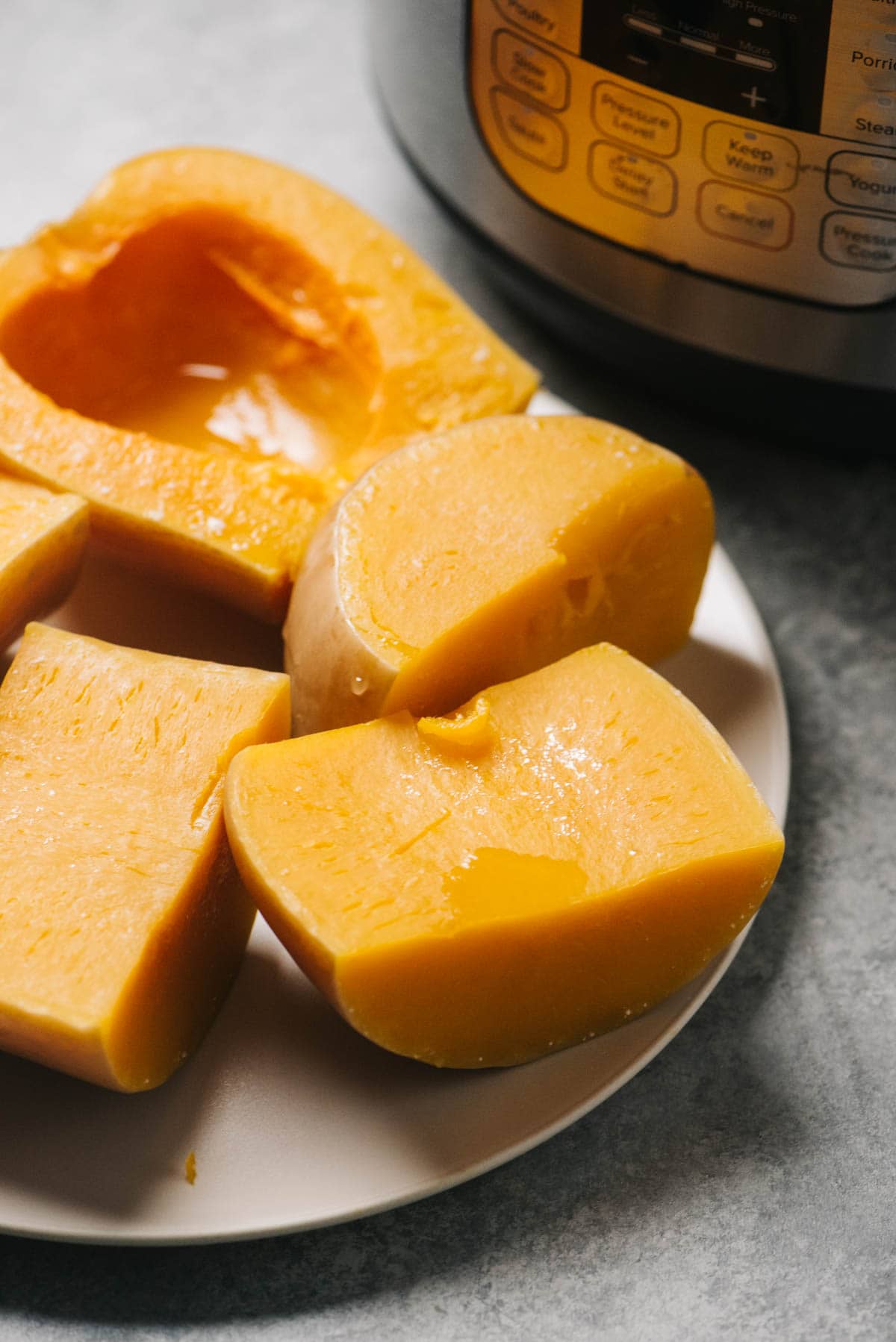 Steamed butternut squash halves on a plate in front of an instant pot.
