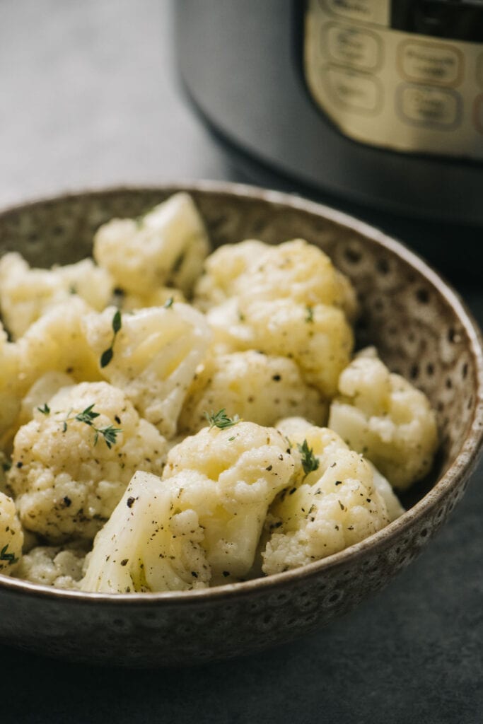 A bowl of steamed cauliflower florets in front of an instant pot.