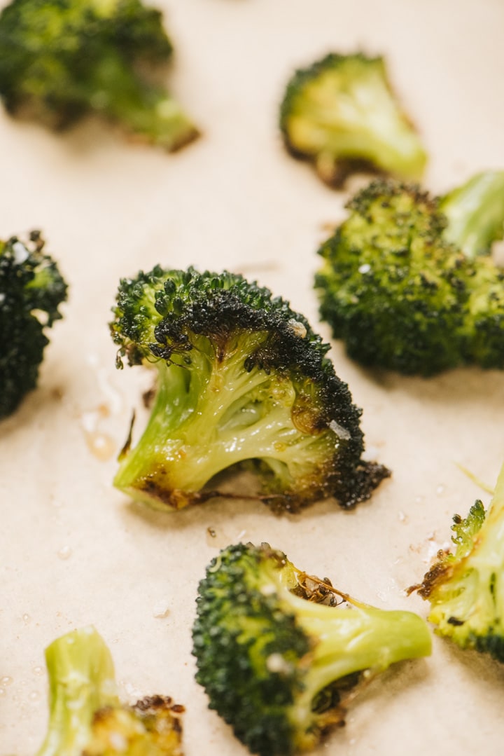 Side view, roasted broccoli florets on a parchment lined baking sheet.