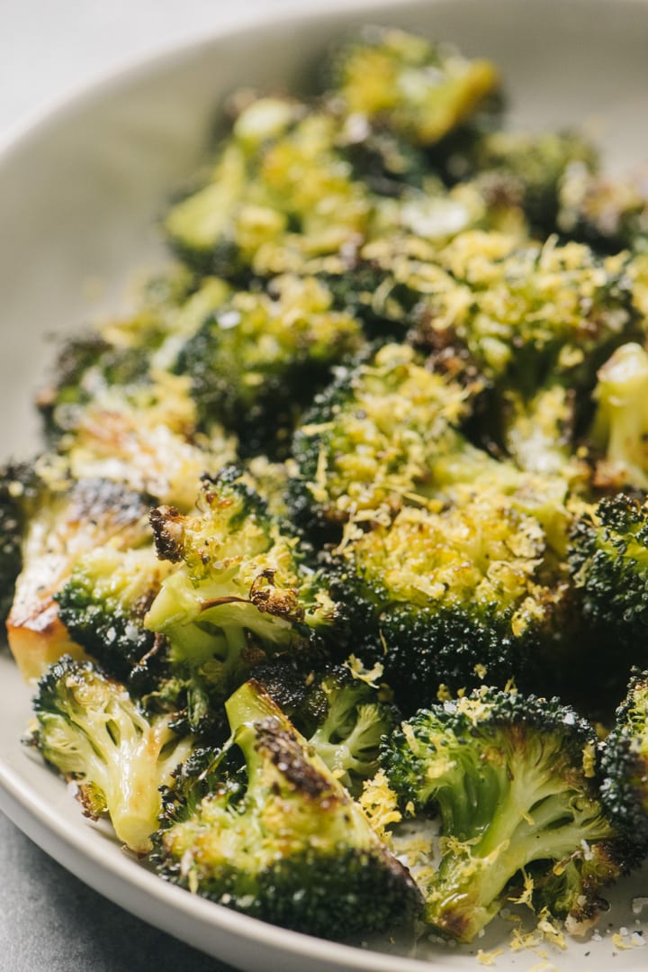 Side view, roasted broccoli in a tan serving bowl seasoned with lemon zest.