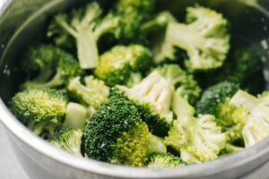 Broccoli florets tossed with olive oil and salt in a metal mixing bowl.