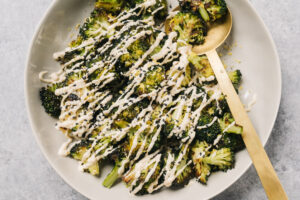 Keto roasted broccoli in a tan serving bowl drizzled with tahini sauce.