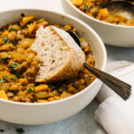 A slice of bread dipped into a bowl of lentil stew.
