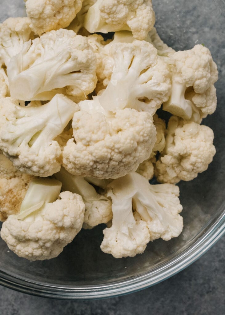 Raw cauliflower florets with water in a microwave safe bowl.