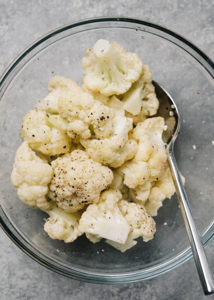 Steamed cauliflower in a glass bowl tossed with olive oil, salt, and pepper.