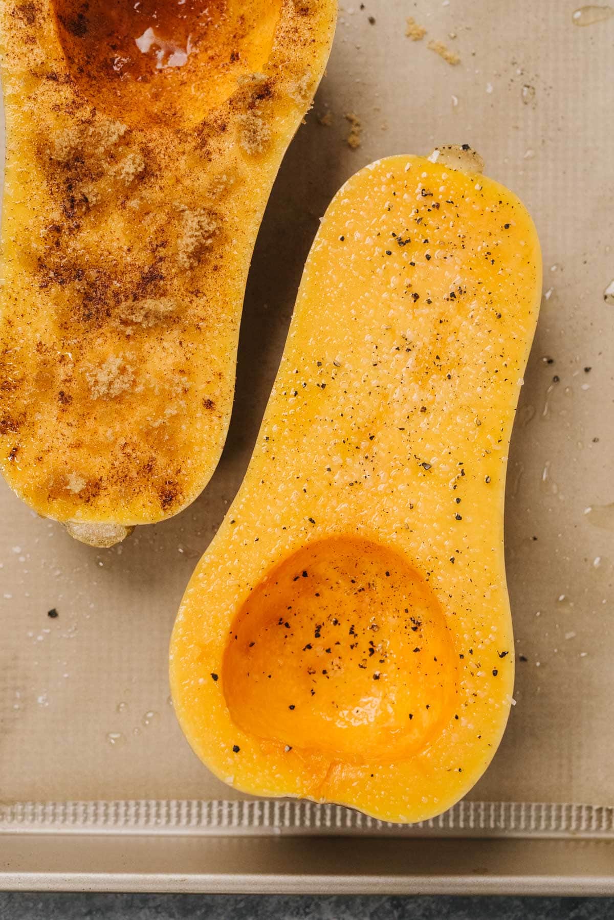 Butternut squash halves drizzled with olive oil, salt, pepper, and seasonings on a parchment lined baking sheet.