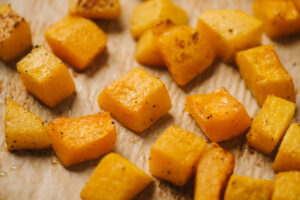 Roasted butternut squash cubes on a parchment lined baking sheet.