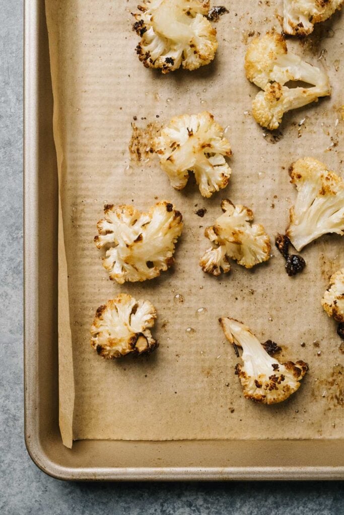 Roasted cauliflower florets on a parchment lined baking sheet resting on a concrete table.