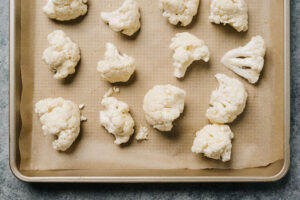 Cauliflower florets tossed with olive oil and salt on a parchment lined baking sheet.