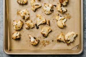 Roasted cauliflower florets fresh from the oven on a parchment lined baking sheet.