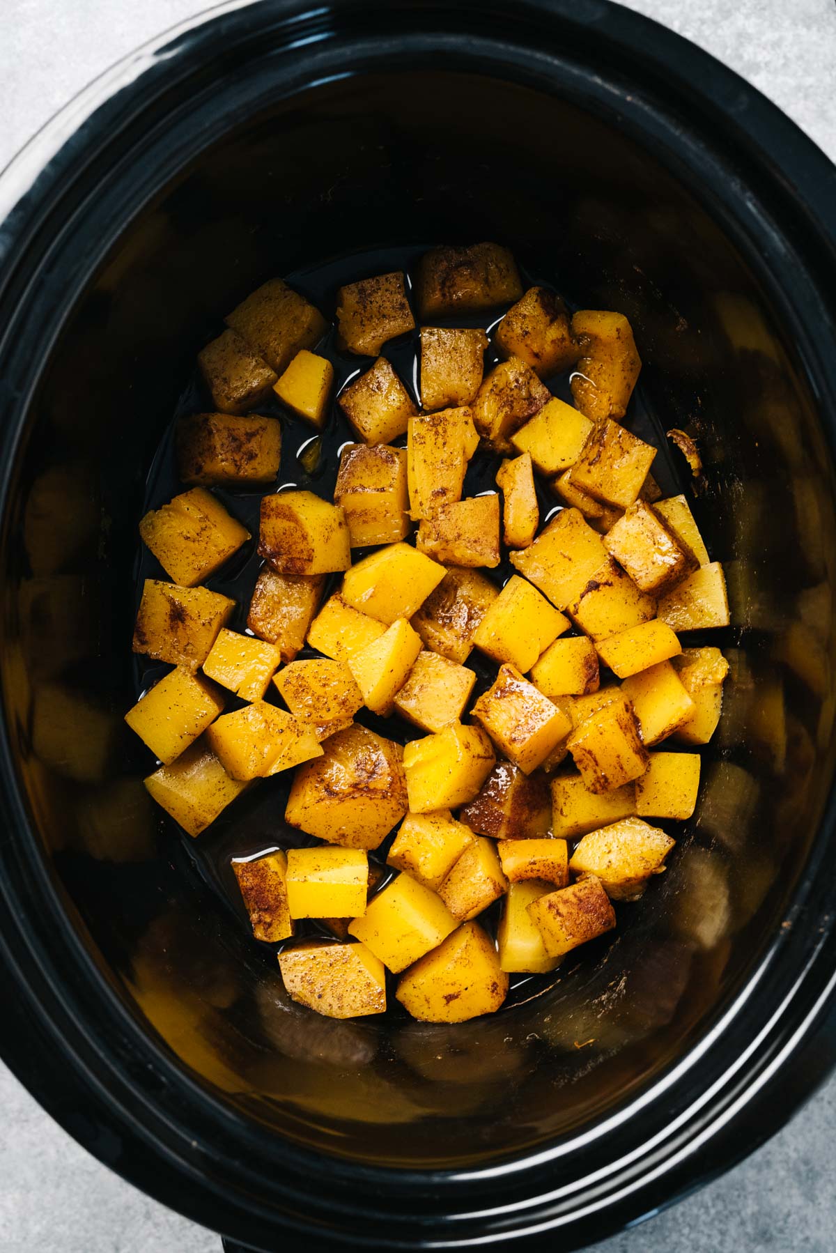 Butternut squash cubes in a slow cooker seasoned with salt, cinnamon, and nutmeg.