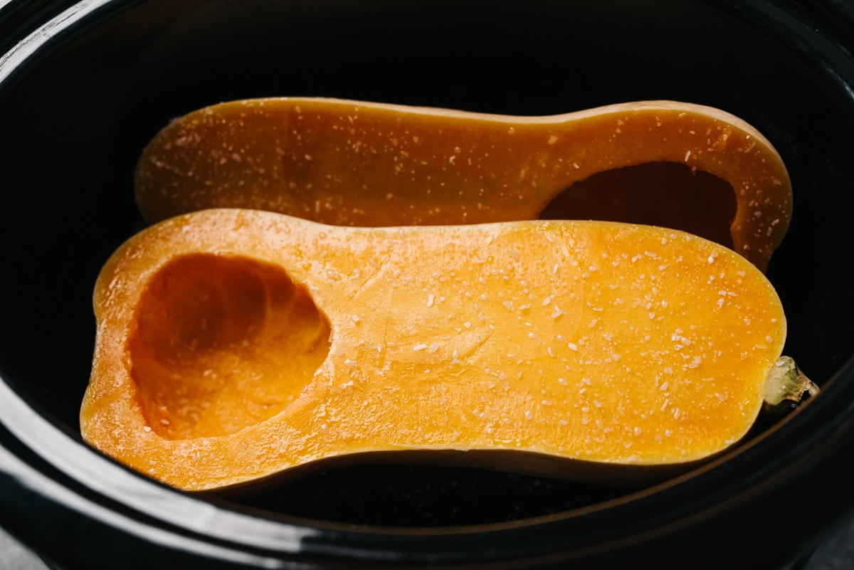 Two halves of butternut squash seasoned with salt in a slow cooker.