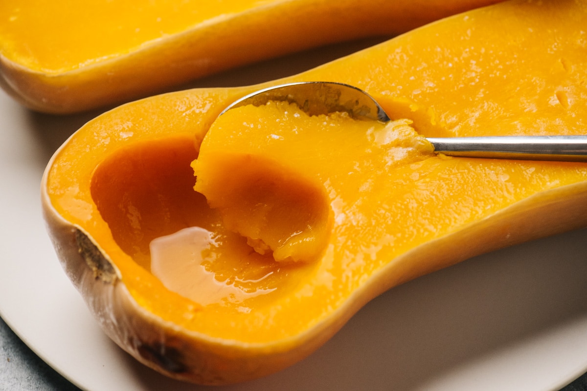 A spoon scooping the flesh from butternut squash cooked in a slow cooker.