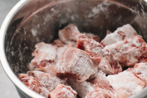 Beef chuck pieces tossed with cornstarch in a large metal mixing bowl.