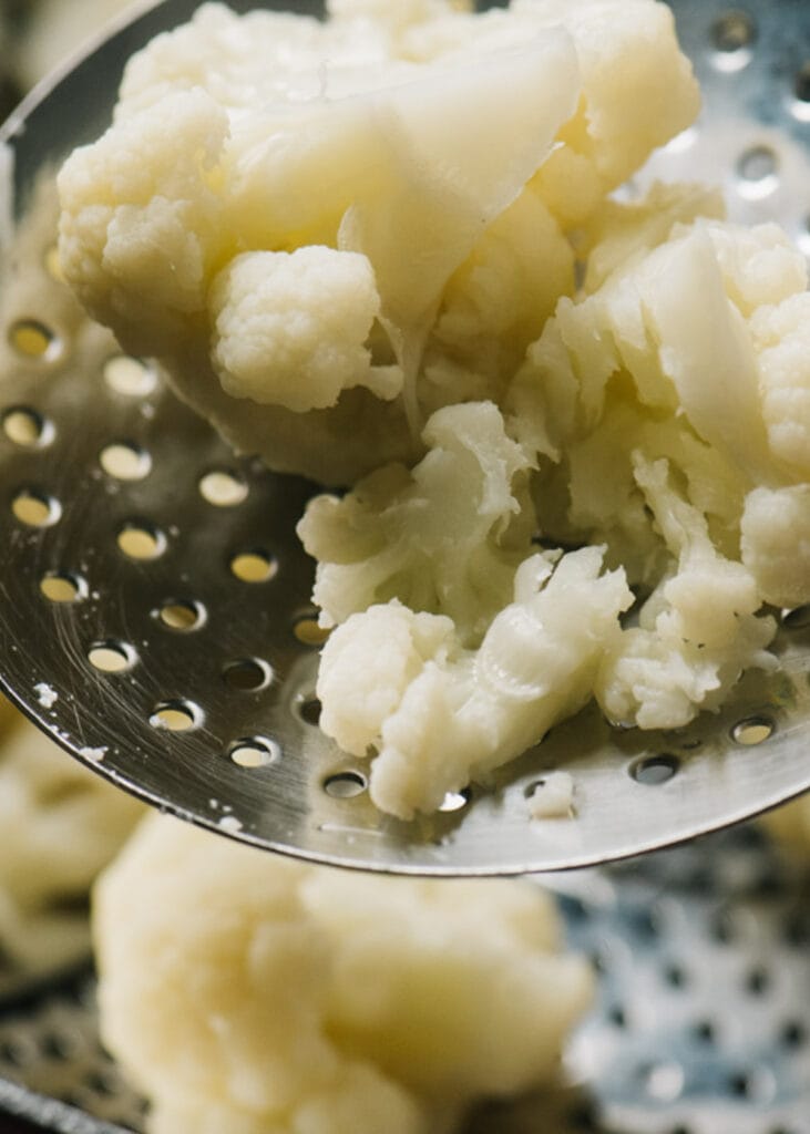 Steamed cauliflower florets on a slotted spoon.