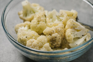 Steamed cauliflower florets tossed with olive oil and seasonings in a glass bowl.