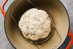 A whole raw head of cauliflower in a red dutch oven on a trivet.