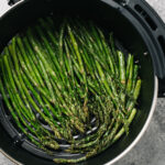 From overhead, cooked asparagus spears in the basket of an air fryer.