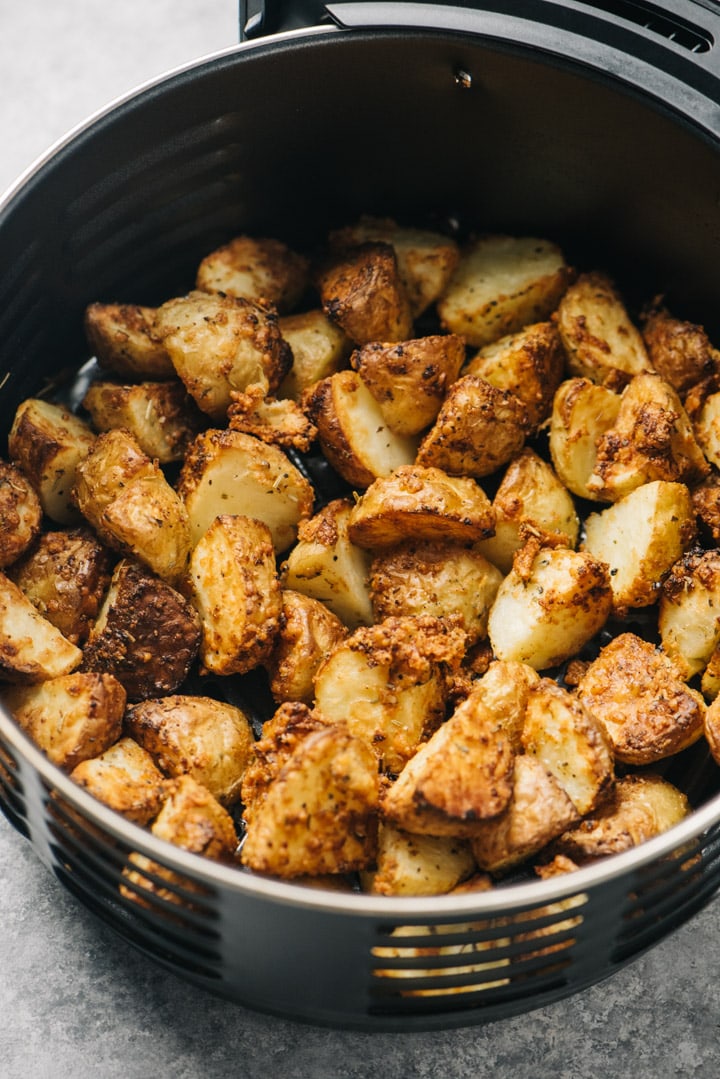 Side view, garlic parmesan potatoes in the basket of an air fryer.