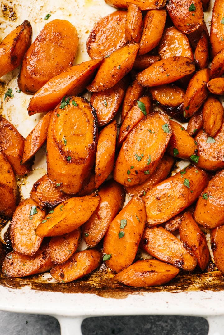 Honey baked carrots in a casserole dish, garnished with finely chopped parsley.