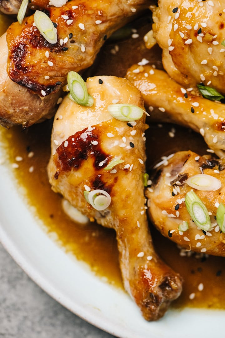 Baked chicken drumsticks with honey garlic sauce on a blue platter, garnished with green onions and sesame seeds.