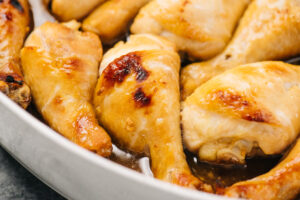 Side view, baked chicken drumsticks with honey garlic sauce in a casserole dish.
