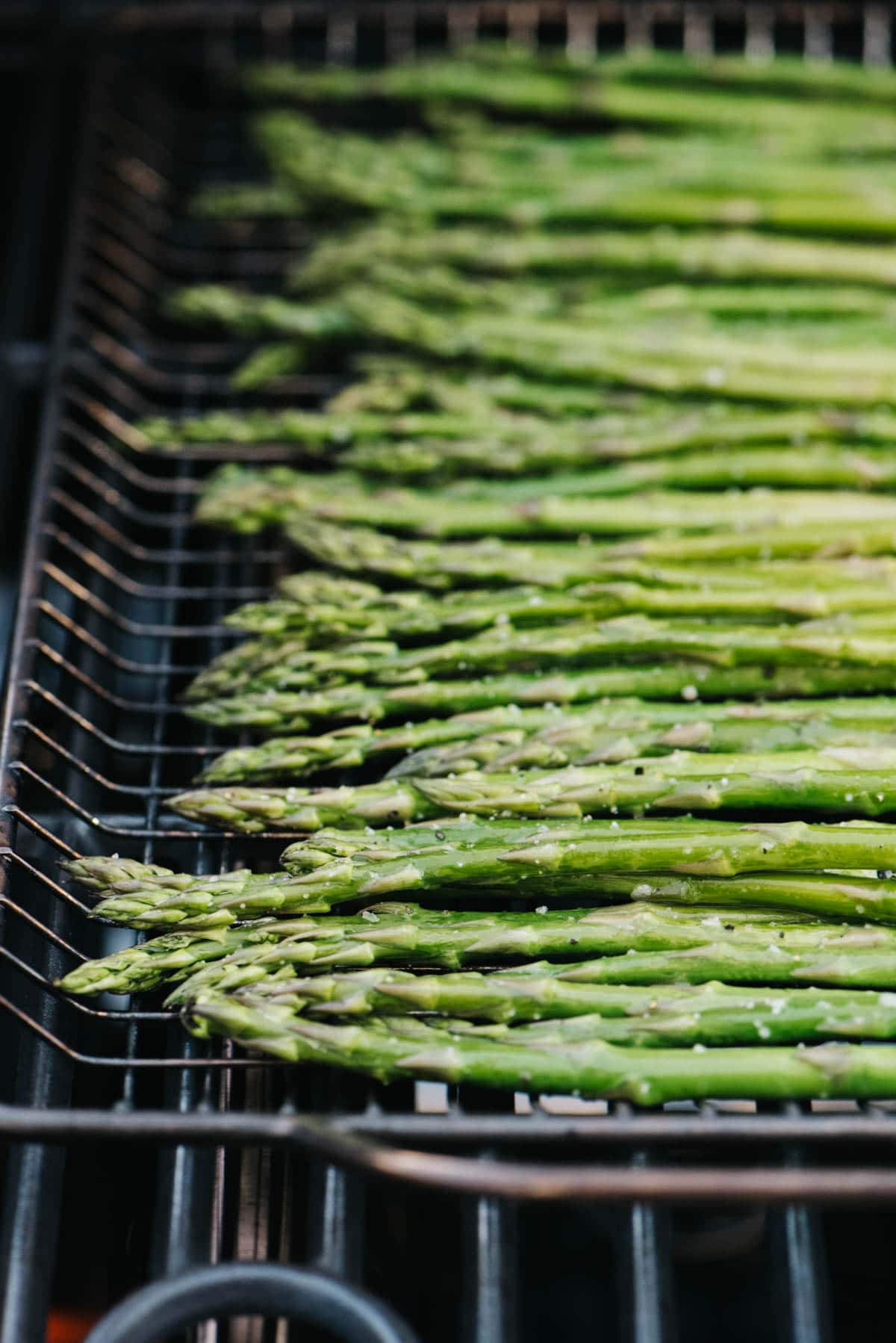Asparagus spears over a grilling basket on a grill.