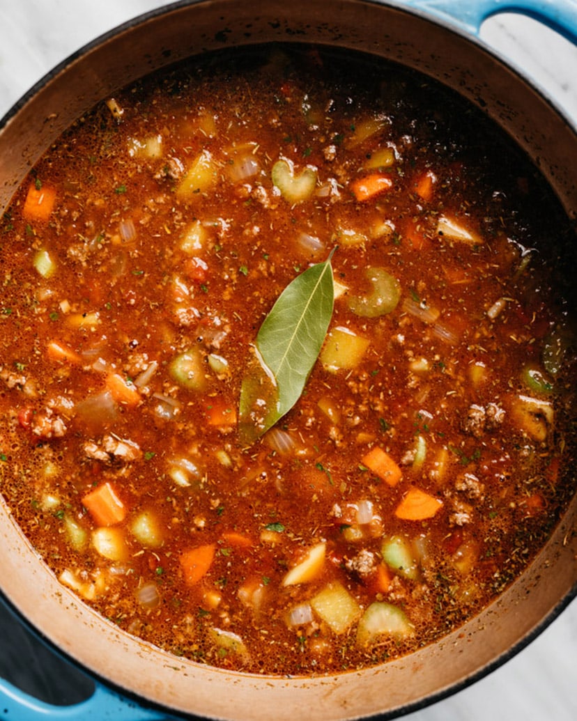Hamburger soup with vegetables and potatoes in a blue soup pot before simmering.