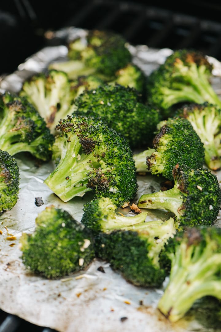 Side view, grilled broccoli florets on a piece of foil over a grill grate.