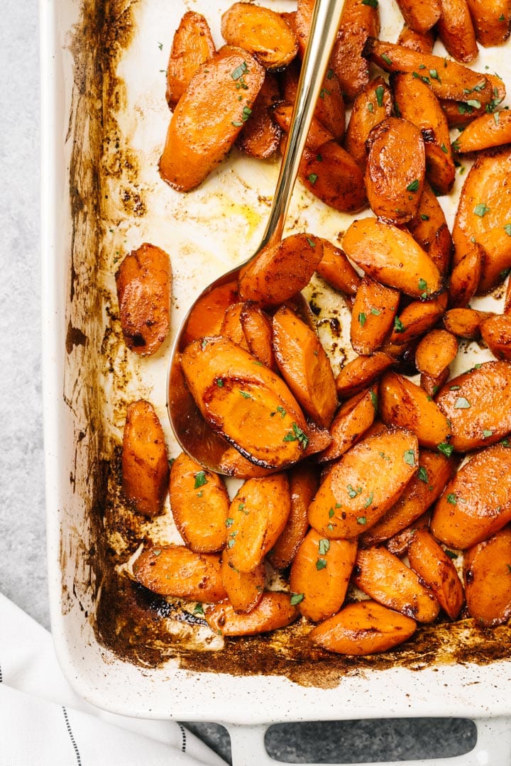 Baked carrots in a casserole dish wit a gold serving spoon.