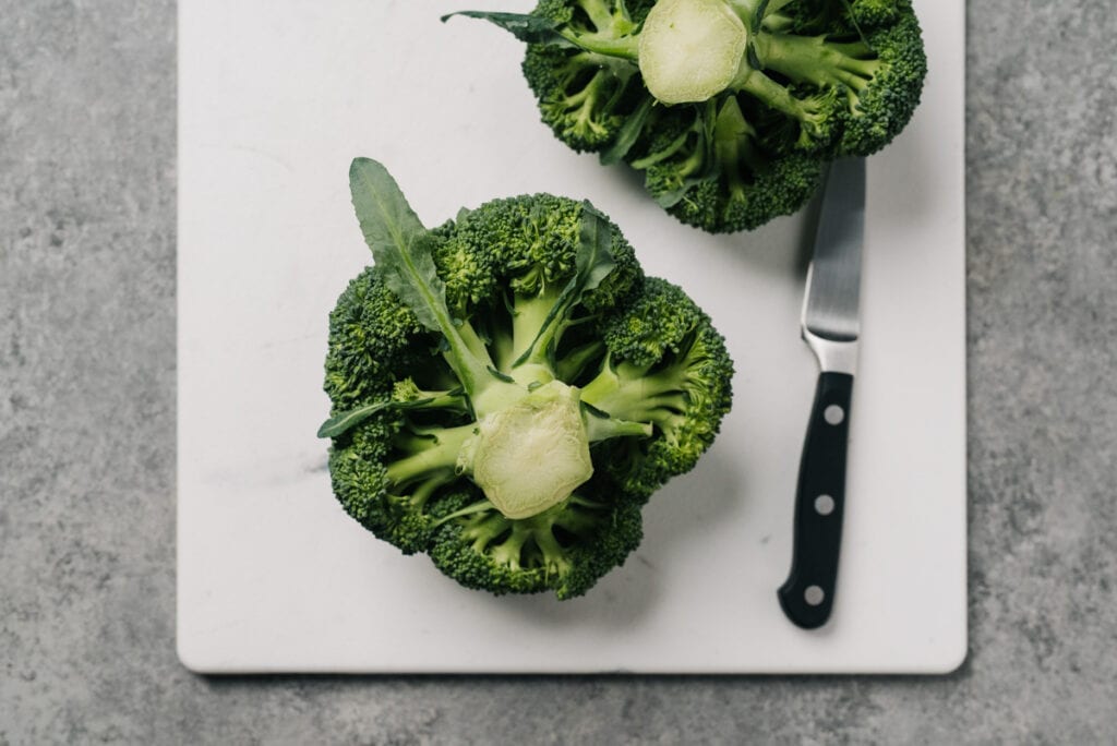 Two heads of broccoli stem side up on a cutting board with a paring knife.