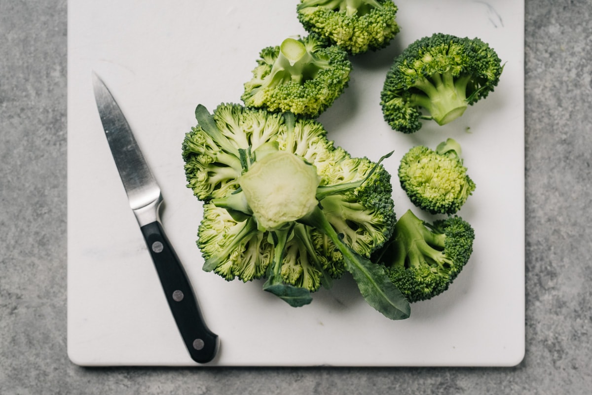 A head of broccoli stem side up with the first row of florets trimmed away using a paring knife.