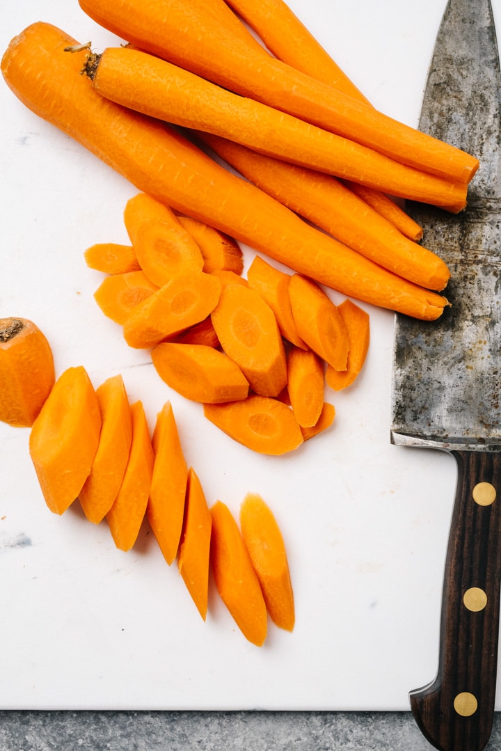 Cutting carrots at an oblique angle on a white cutting board with a large chef's knife.
