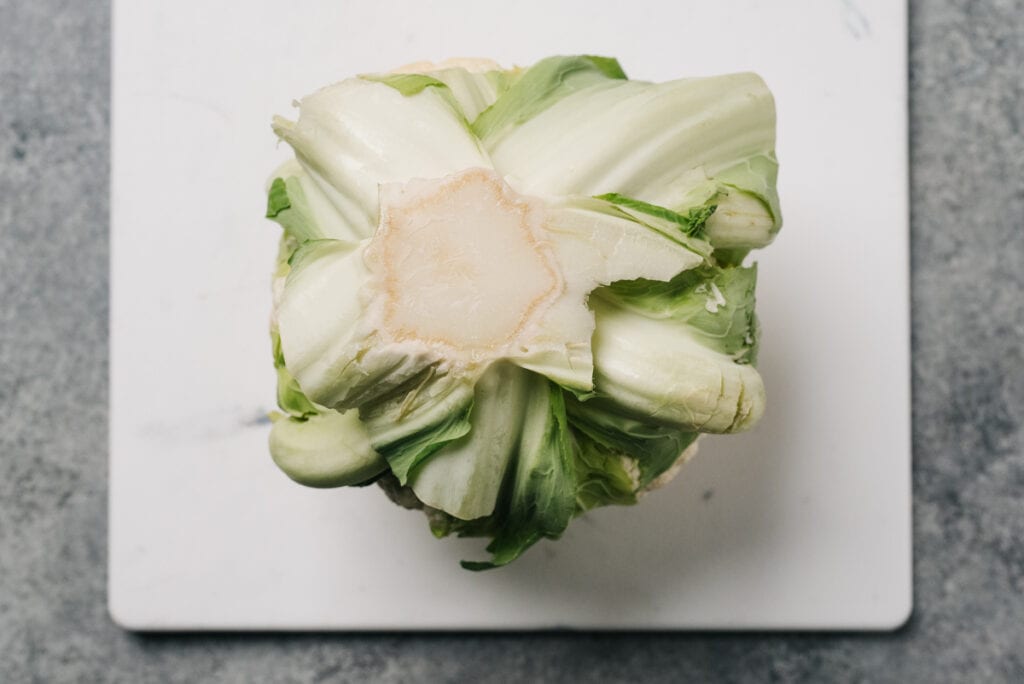 A head of cauliflower on a cutting board stem side up.