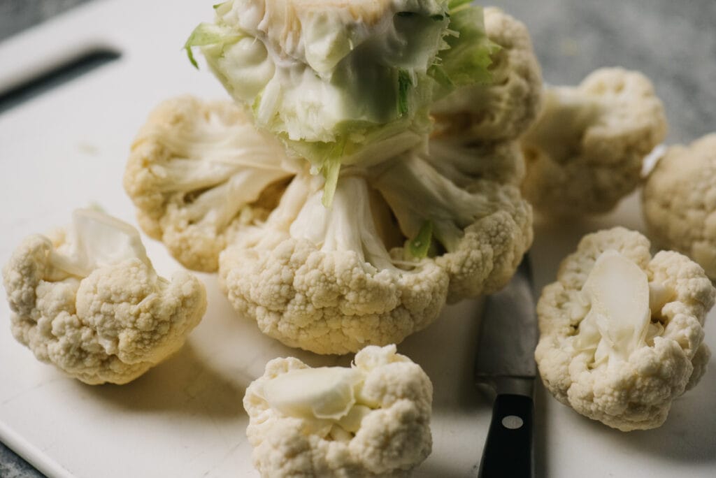 A head of cauliflower on a cutting board with the bottom layer of florets sliced off.