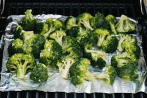 Broccoli florets on a piece of foil over grill grates.