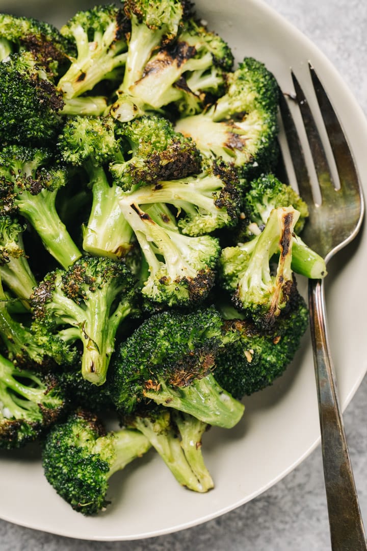 Grilled broccoli florets in a tan serving bowl with a silver serving fork.
