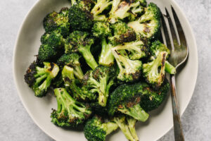 Grilled broccoli florets in a tan mixing bowl with a silver serving fork.