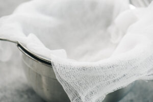 Cheesecloth lining a fine mesh sieve, nested in a mixing bowl.