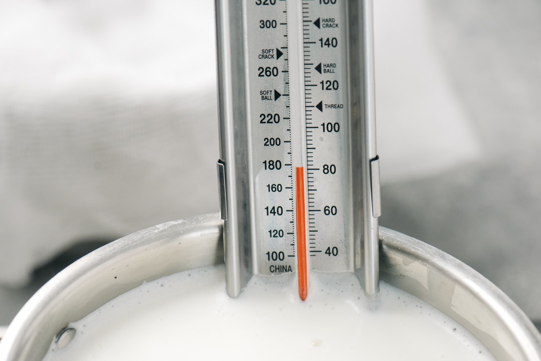 A thermometer in a pot of milk showing a temperature of 180°F.