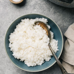 A blue serving bowl of instant pot jasmine rice with a pressure cooker off to the side and a tan linen napkin.