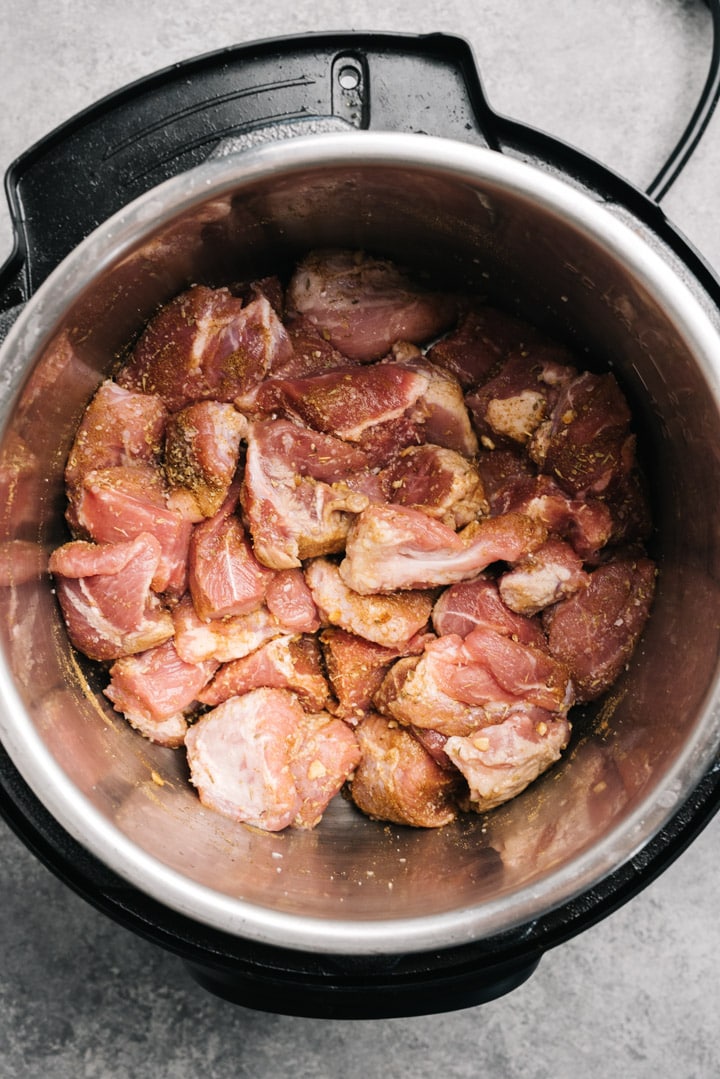 Chunks of pork shoulder tossed with minced garlic, salt, cumin, and oregano in an instant pot.