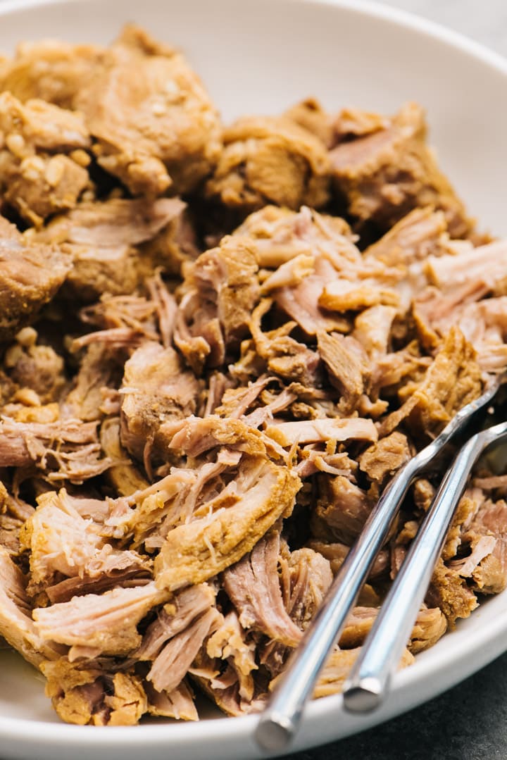 Side view, shredded instant pot carnitas in a white bowl with two forks.