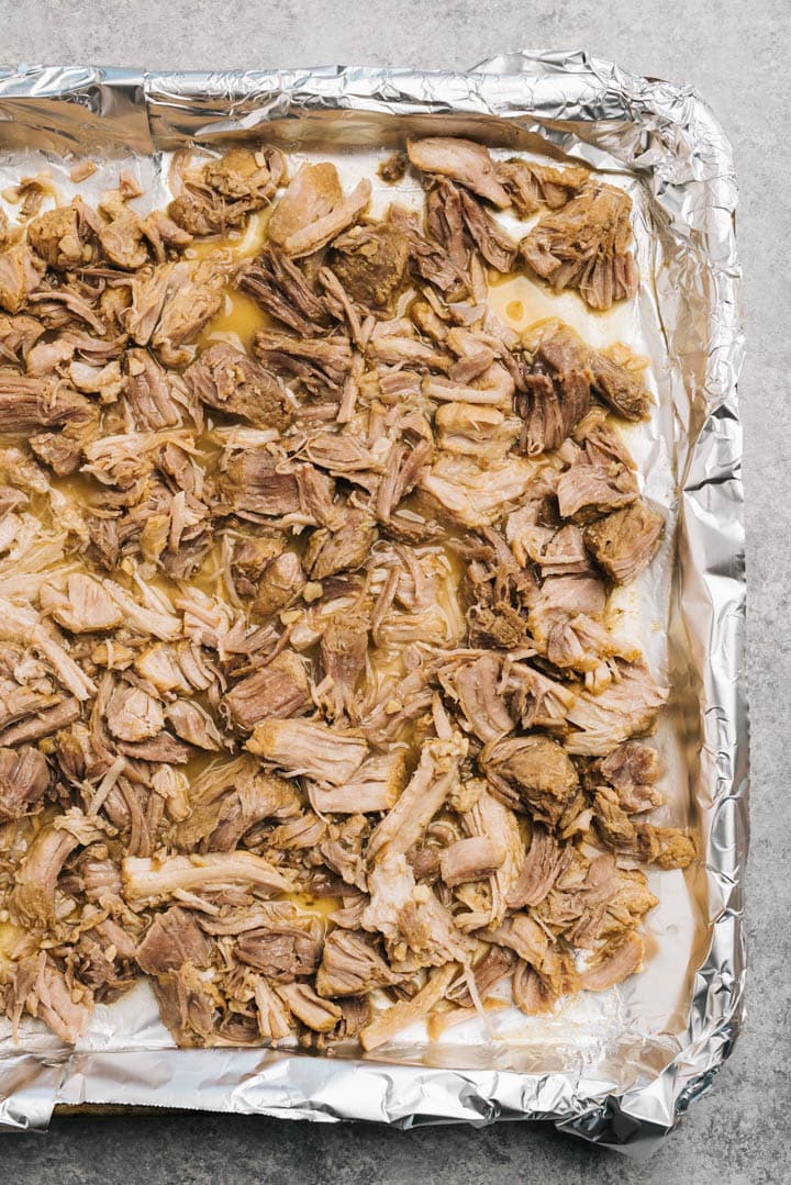 Shredded pork carnitas on a foiled lined baking sheet drizzled with pan juices.